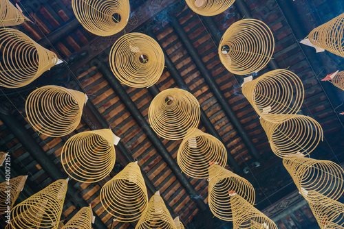 Traditional incense spiral sticks in a temple. Multiple yellow shapes and structures, hung from the ceiling. Religion, spirituality.
