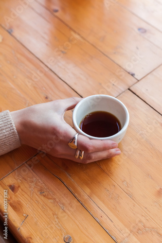 woman holds in hand a ceramic mug with black coffee. alternative brewing of specialty coffee. background light wood