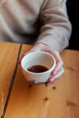 woman holds in hand a ceramic mug with black coffee. alternative brewing of specialty coffee. background light wood