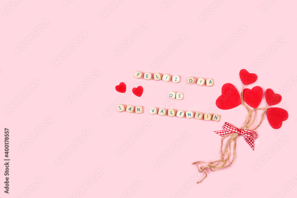 Feliz día de San valentín escrito en unos cubos de madera junto a unos corazones rojos sobre un fondo rosa liso y aislado. Vista superior. Copy space