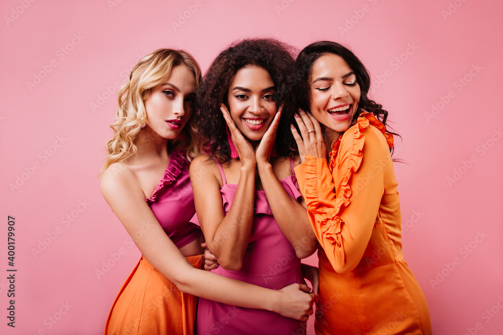 Three cute girls posing together on pink background. Half length portrait of international female models. Three cute girls posing together on pink background. Half length portrait of international female models.
