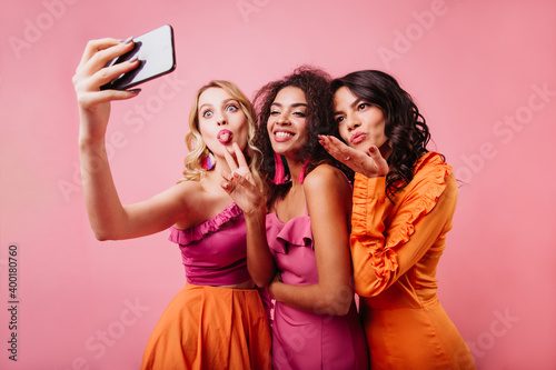 Latin happy girl sending air kiss. Charming ladies making selfie on pink background.