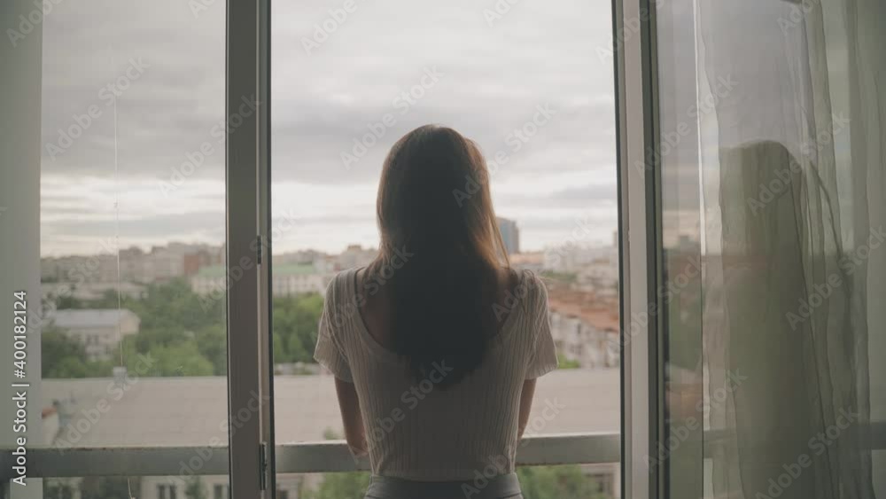 Young woman stands and looks out the window, happy confident lady Young woman stands and looks out the window, happy confident lady