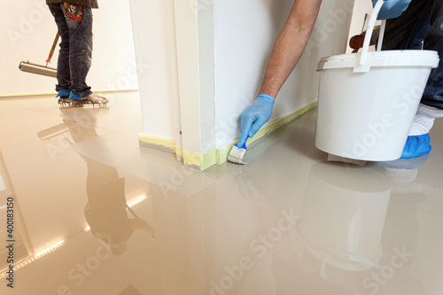 Close-up of construction workers applying a new layer of an indoor synthetic cast coating floor around the edges with a paint brush.