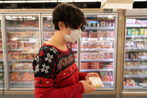 shopping woman wearing medical mask short hair at the grocery store for christmas or new year dinner table. cheese, ugly christmas sweater. coronavirus times pandemic. blurry photo. diversity. 2021