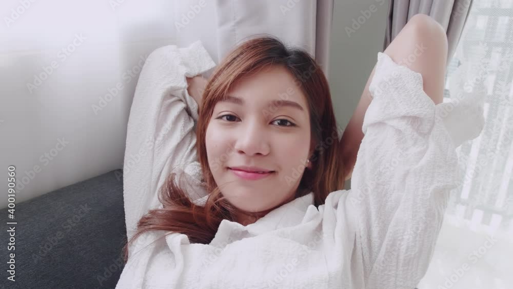 A cute Asian woman lying back and playing on the sofa in the living room resting happily on vacation at home. A cute Asian woman lying back and playing on the sofa in the living room resting happily on vacation at home.