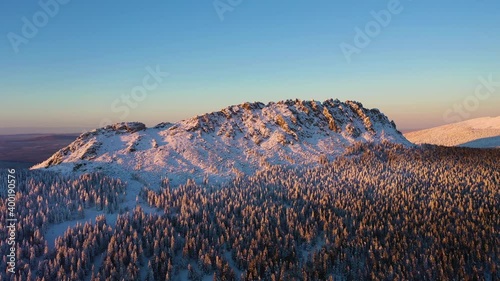 Otkliknoy Mountain Ridge and Coniferous Forest at Sunset in Winter. Aerial View. Taganay National Park, Southern Urals, Russia. Drone Flies Forward photo