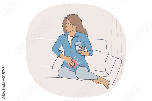 Menstruation pain concept. Young stressed female sitting on bed with glass of water, touching belly and suffering from pain of menses periods at home. Gynecology calendar and pms symptoms 