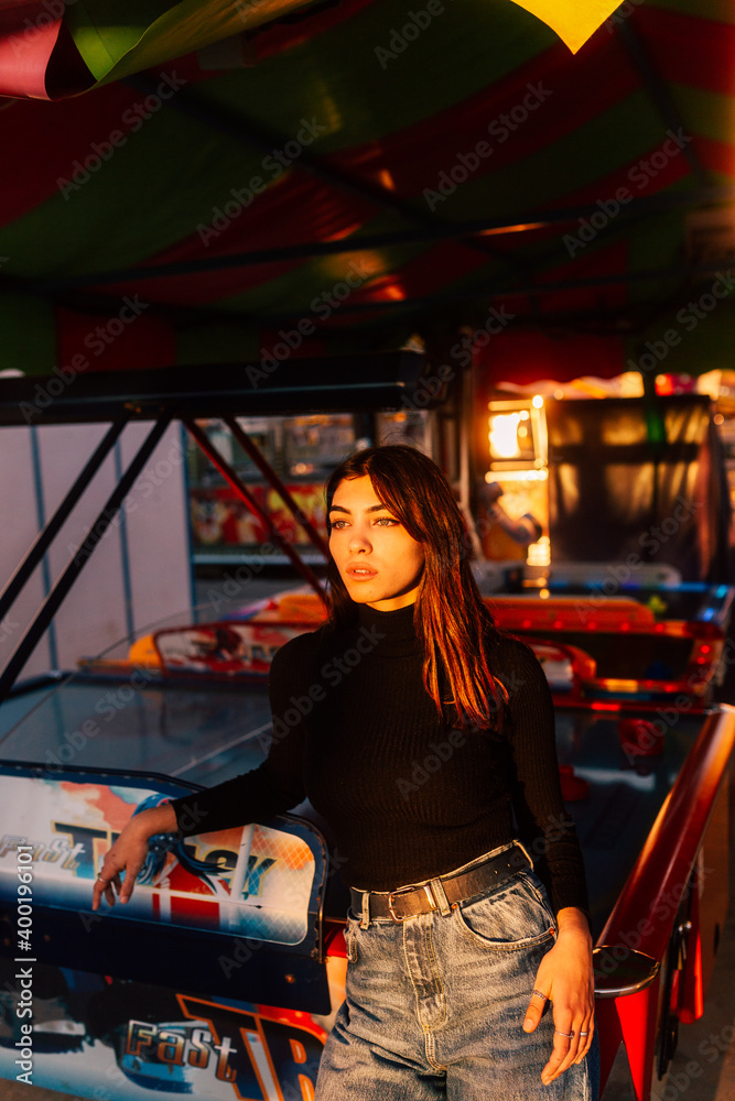 attractive brunette girl with green eyes posing with a colorful amusement park background with lights