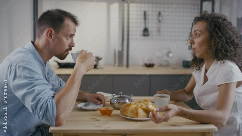 Medium shot of emotional stressed woman shouting at her husband while having breakfast together sitting in front of each other at kitchen table Medium shot of emotional stressed woman shouting at her husband while having breakfast together sitting in front of each other at kitchen table