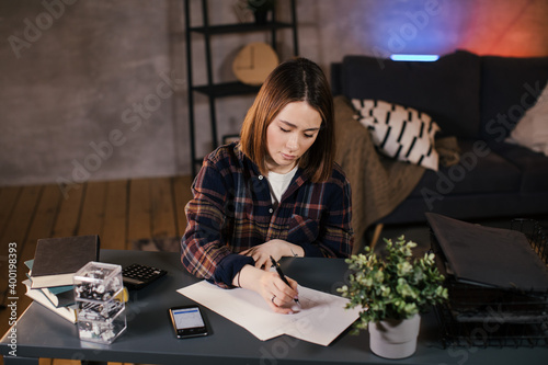 Asian girl trader working at home at the table, studying the chart