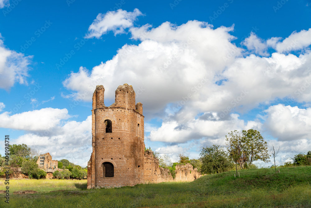 Panorama of the Circus of Maxentius Appia Antica, of the brick tower that stands out majestically among the clouds and the blue of the sky and the green of the lawn on a bright day. Rome Italy.