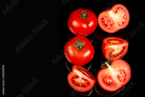 large red tomatoes and cut halves on a black background