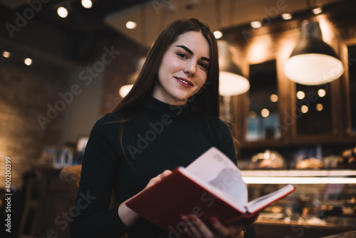 Cheerful young woman with book smiling at camera