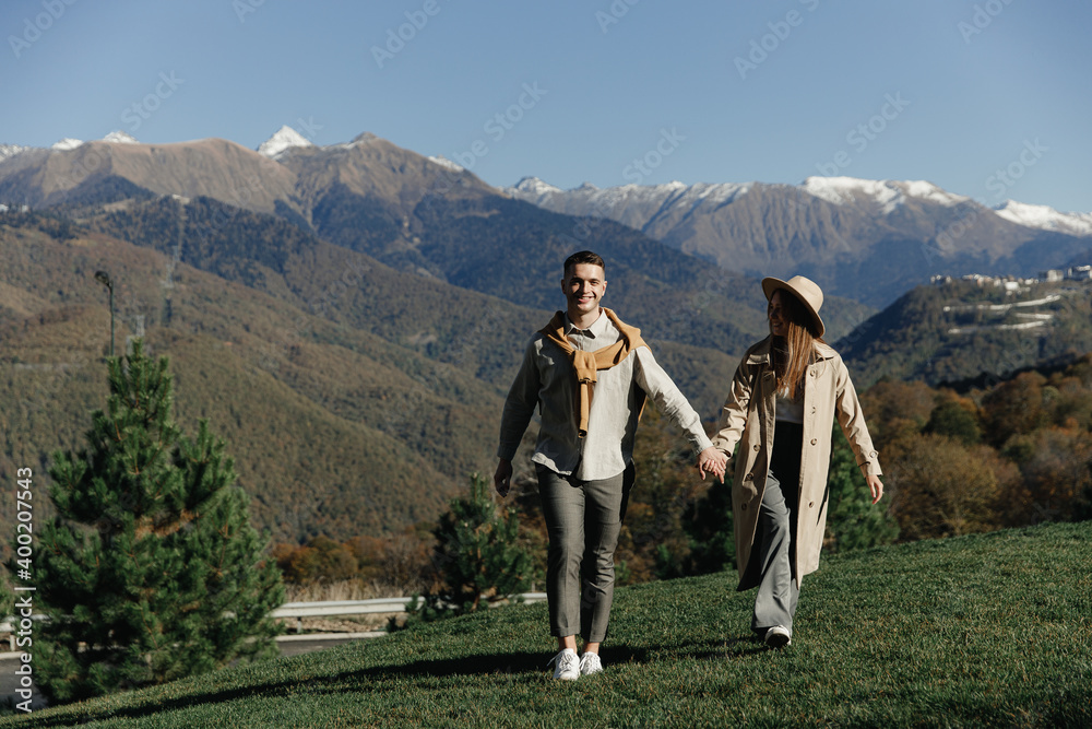 Happy couple in love are walking in fashion autumn clothes on the background of nature mountains landscape, holding hands and having fun. Date when quarantine and self-isolation Happy couple in love are walking in fashion autumn clothes on the background of nature mountains landscape, holding hands and having fun. Date when quarantine and self-isolation