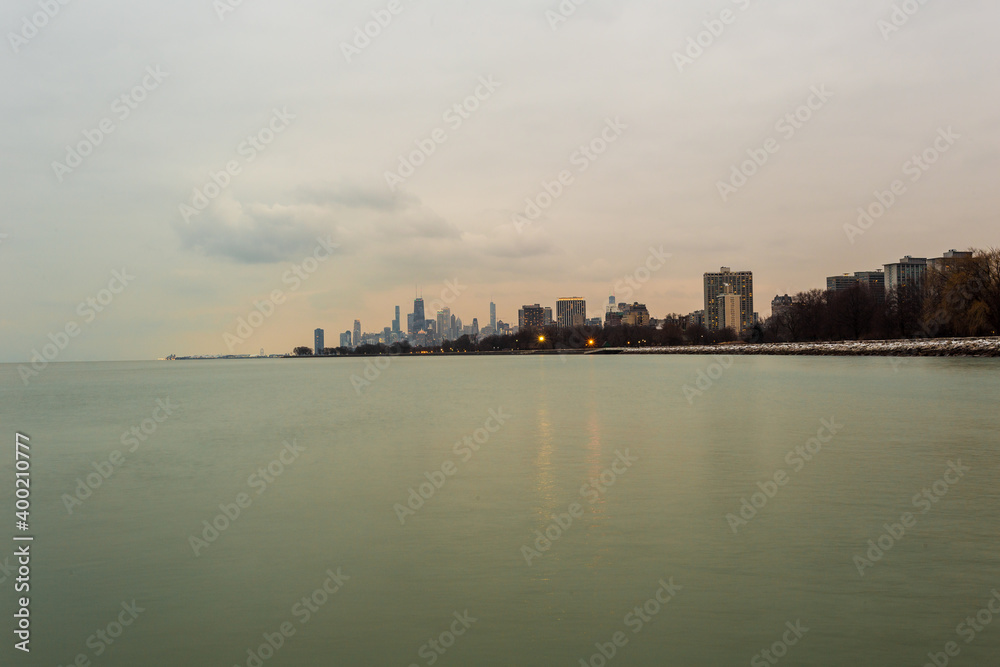 Chicago skyline in the distance with calm lake and sunset light on cloudy evening