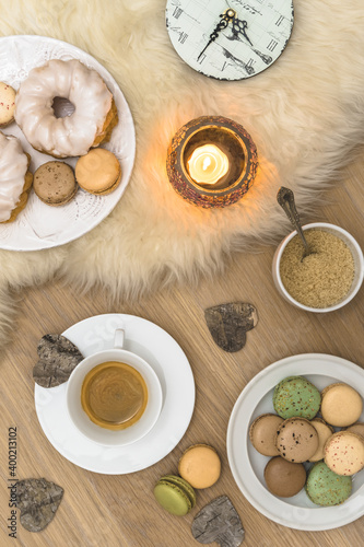 Scene of a cozy coffee break with macarons, donuts, biscuits and candle on lambskin and wood