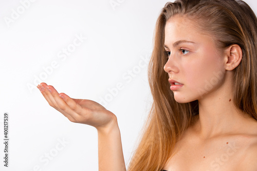 Cute blonde with gentle skin, looks at her outstretched empty hand on a white background. Naturally beauty concept and cosmetic product advertisment