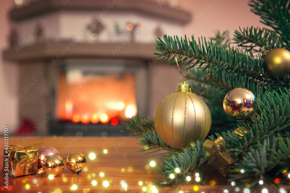 Christmas background with golden bauble , fireplace and decorated fir tree branch.