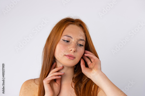 Beauty, spa and glowing skin concept. The red-haired girl poses and looks at the floor on white background.