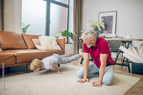 Grey-haired fit man doing yoga with son and looking strong