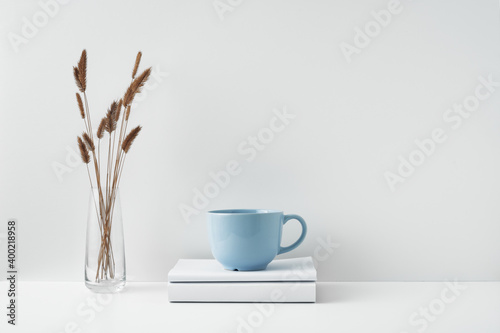 A mug on a stack of books and a transparent vase with dried flowers. Eco-friendly materials in interior decor, minimalism. Copy space, mock up.