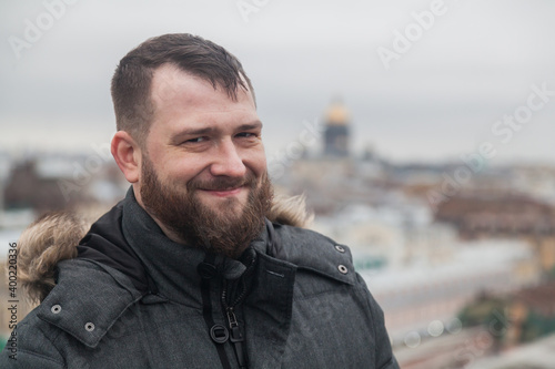 Dark-haired bearded man in a winter jacket against the backdrop of city rooftops