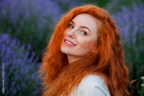 Summer portrait of a beautiful girl with long curly red hair. European girl in lavender field. Wavy Red Hair