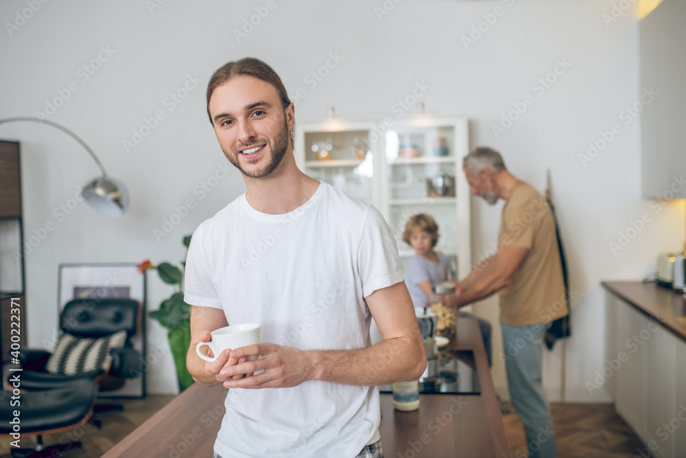 Young man in white tshirt standing in the kitchen and smiling Young man in white tshirt standing in the kitchen and smiling