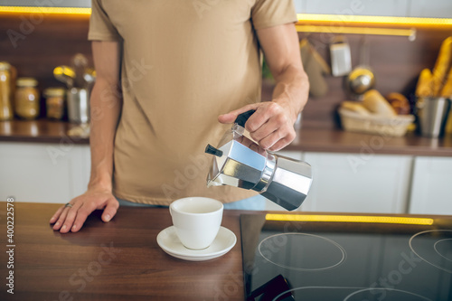 Close up of a man in beige tshirt pouring coffee to the cup