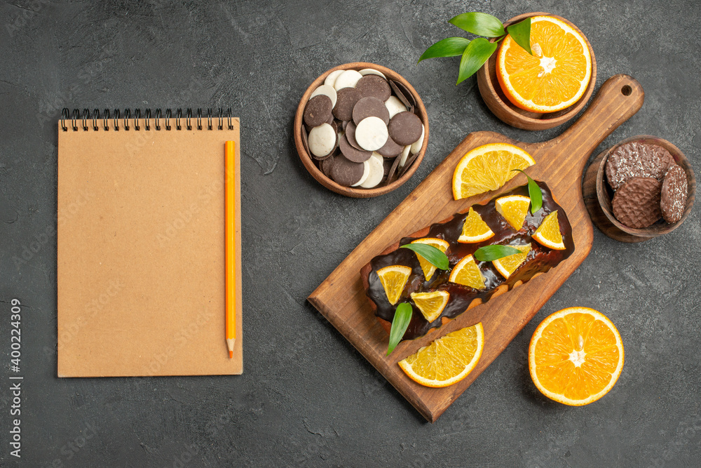 Tasty cakes cut lemons with biscuits next to notebook on cutting board on dark table