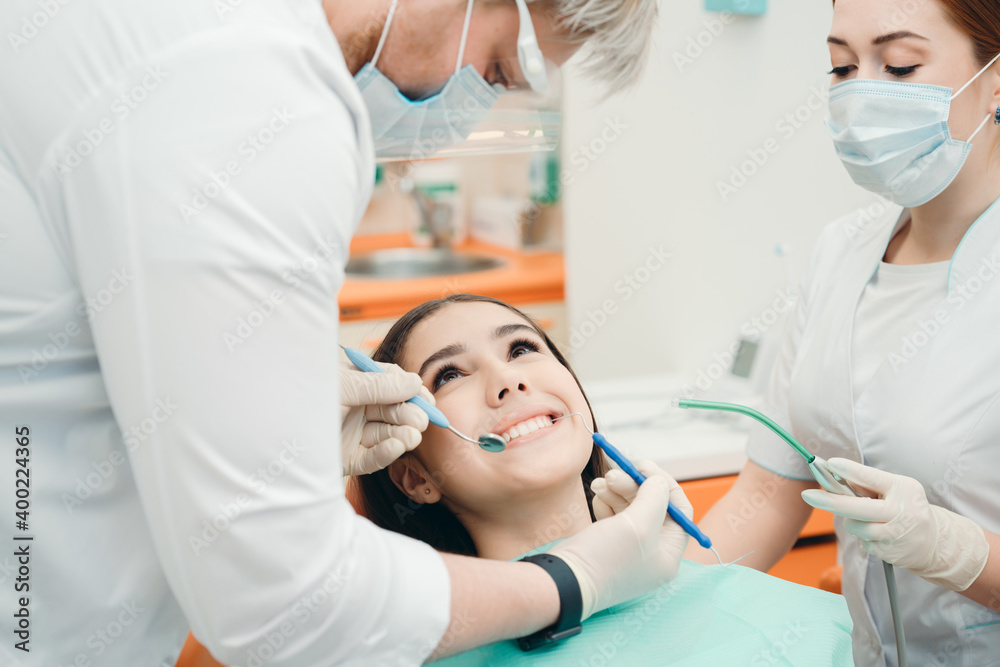 Smiling brunette lying in the dental office while doctors perform the procedure Smiling brunette lying in the dental office while doctors perform the procedure