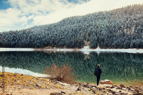 man walk in winter forest covered snow. tourist man travel to snowy mountains background. Winter lake with pine forest and mountains.