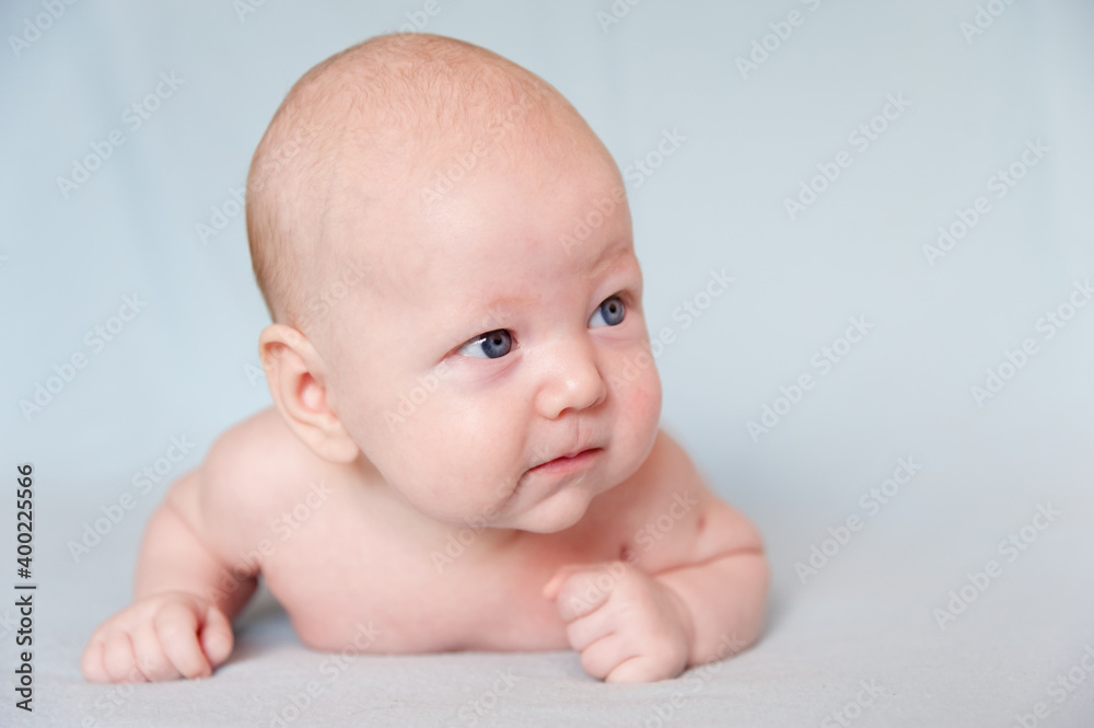 A smiling baby newborn boy with blue eyes smiles and crawls on a white sheet. A smiling baby newborn boy with blue eyes smiles and crawls on a white sheet.