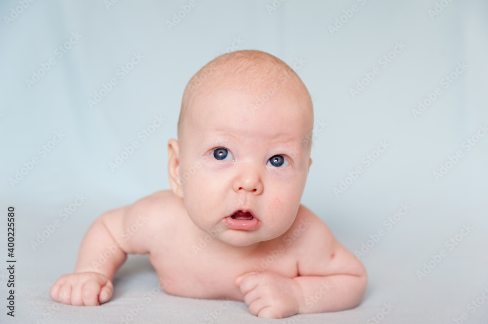 A smiling baby newborn boy with blue eyes smiles and crawls on a white sheet. A smiling baby newborn boy with blue eyes smiles and crawls on a white sheet.
