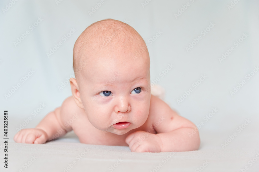 A smiling baby newborn boy with blue eyes smiles and crawls on a white sheet. A smiling baby newborn boy with blue eyes smiles and crawls on a white sheet.