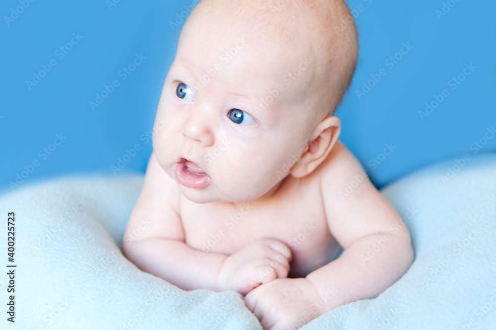 A smiling baby newborn boy with blue eyes smiles and crawls on a white sheet. A smiling baby newborn boy with blue eyes smiles and crawls on a white sheet.