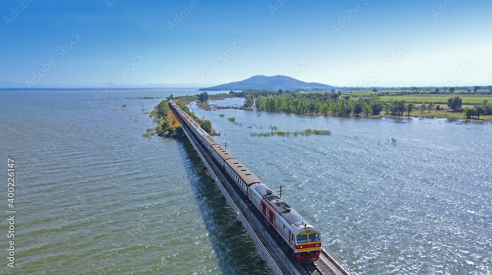 Aerial view of Thailand travel train running into the floating railway bridge with blue sky in the lake of 