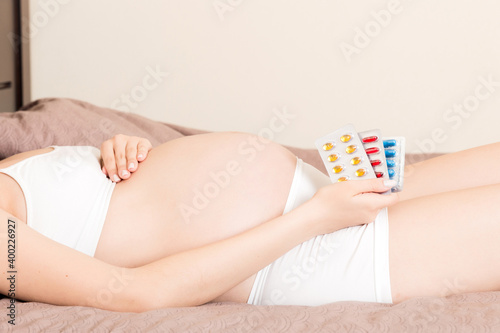 Midsection of pregnant woman taking vitamin pill on sofa at home © sosiukin