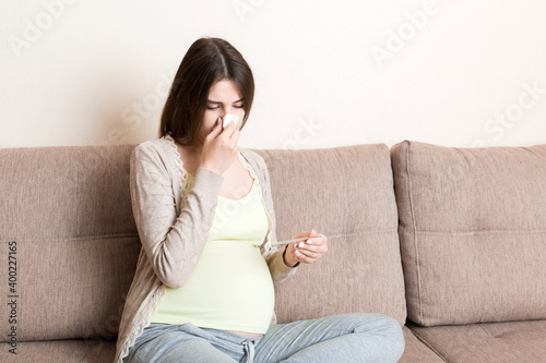 Sick pregnant woman blowing nose into tissue at home Healthy millennial healthcare concept