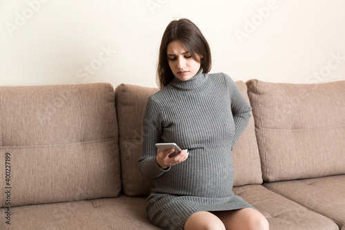 Portrait of pregnant woman in pain on sofa at home, making phone call