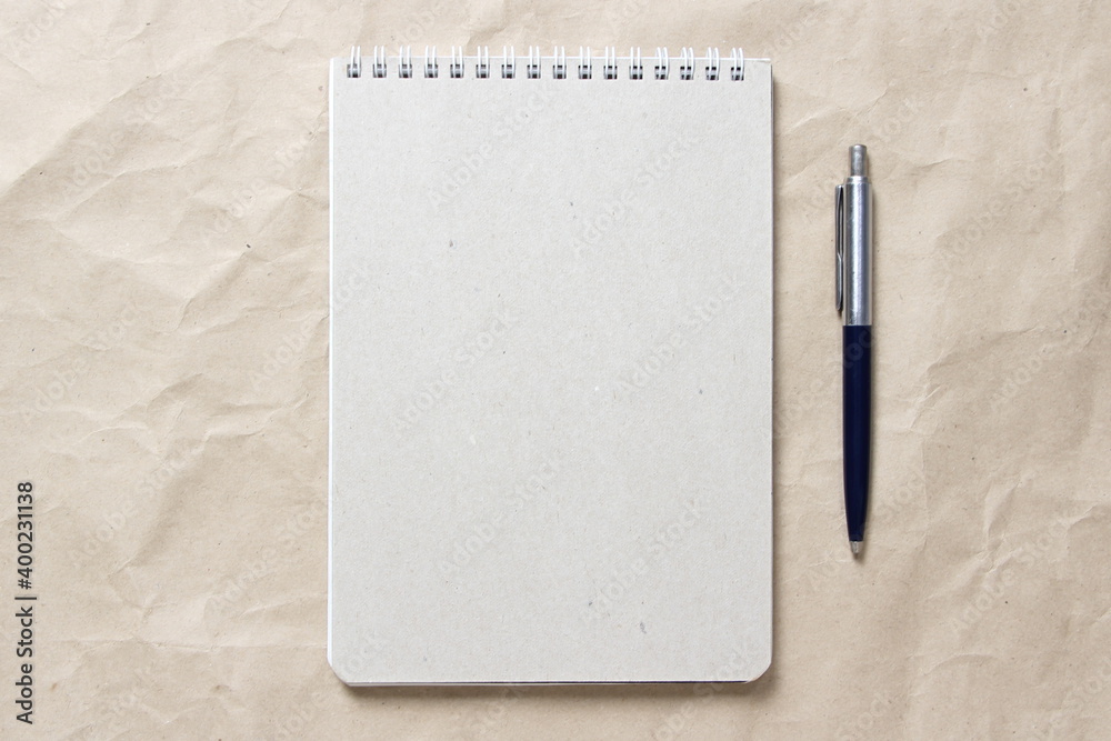 Gray notepad with white coiled spring and pen on a background of beige crumpled craft paper Gray notepad with white coiled spring and pen on a background of beige crumpled craft paper