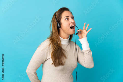 Young telemarketer woman over isolated blue background shouting with mouth wide open to the side