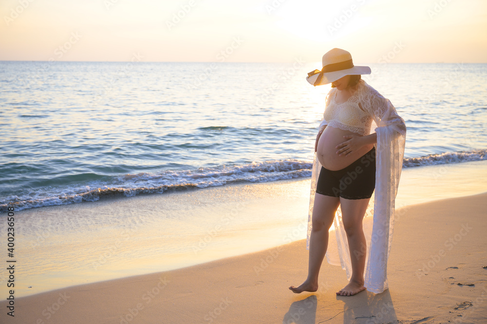 Young Asian pregnant woman relaxing walking on the beach at sunset