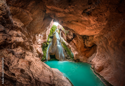 A beautiful waterfall inside a cave and a lake of crystal clear turquoise water. Enchanted landscape, a cave inside a mountain in which there is a waterfall and a crystalline river. Bercolon waterfall © Hector