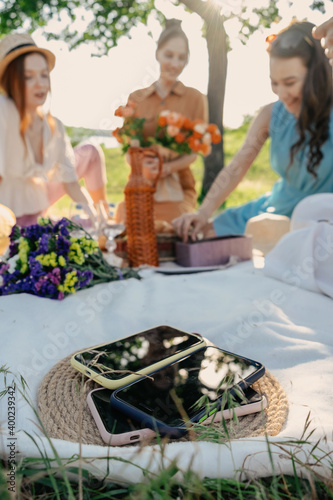 Digital Detox, time for disconnecting from electronic devices. Mobile phones on basket on picnic background. Group of young woman hanging out together on a picnic in nature at no phone zone