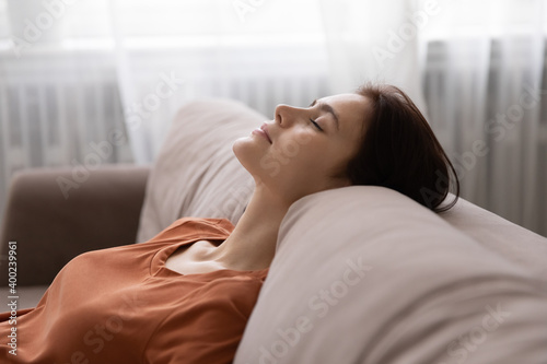 In harmony with myself. Serene millennial woman spending time at home taking break for rest relax. Tranquil young lady lean back on couch in comfortable pose, dream with closed eyes, breath fresh air photo