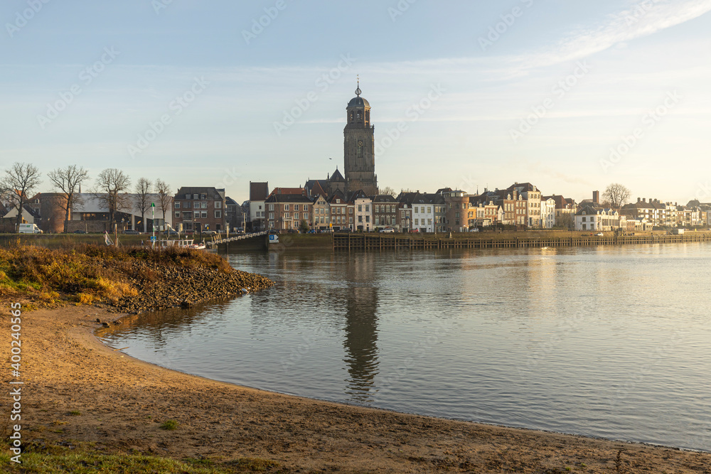 Beach lit up by early morning sun in the foreground and cityscape of the Dutch Hanseatic medieval city of Deventer in The Netherlands seen from the other side of the river IJssel behind