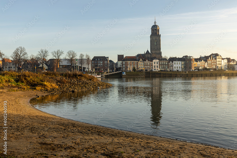Beach in the foreground and cityscape of the Dutch Hanseatic medieval city of Deventer in The Netherlands seen from the other side of the river IJssel at sunrise