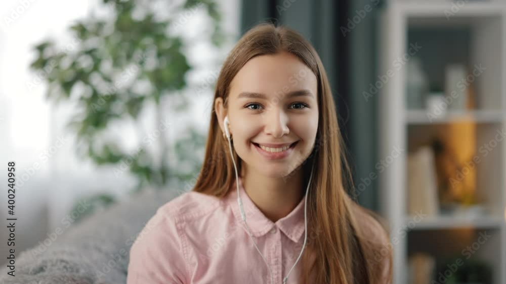 First person view of smiling young female talking and waving during video conversation at home. Happy brunette having online communication while sitting on couch.